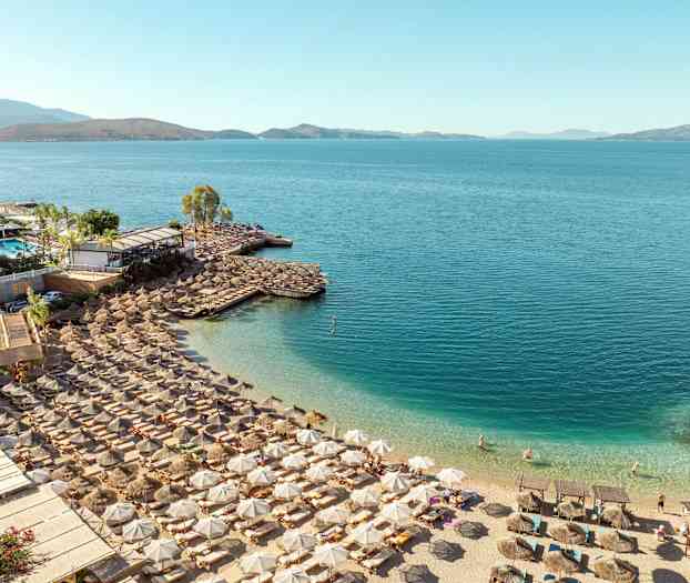 Strand med solsenger, parasoller og en klarblå havutsikt. (AI-generert tekst)