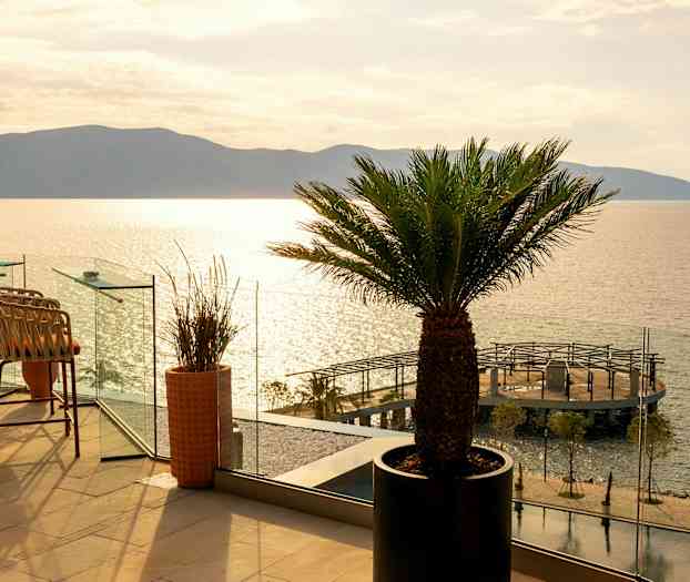 En terrasse med stoler og palmer og utsikt over havet og en brygge. (AI-generert tekst)