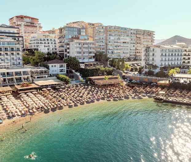 Hotell og parasoller ved en strand med klart vann. (AI-generert tekst)