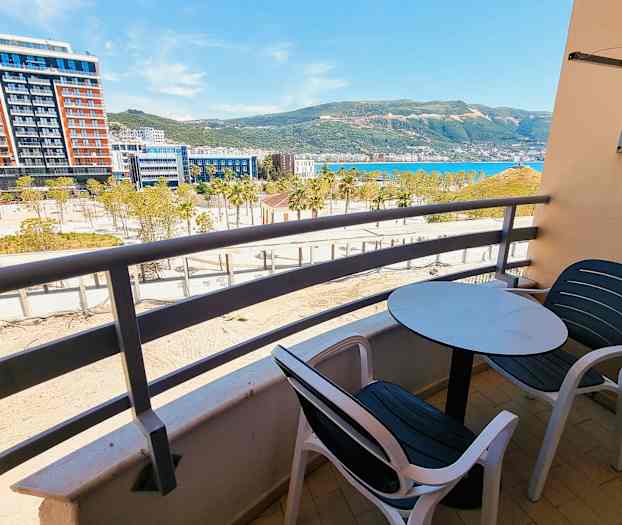 En balkong med bord og stoler med utsikt over et bygningsområde, by og fjell. (AI-generert tekst)