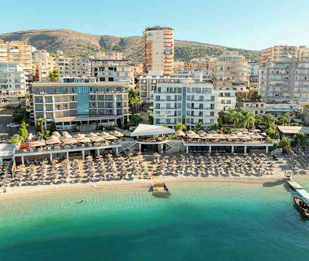 Utsikt over en strand med solsenger og hotellbygninger i bakgrunnen. (AI-generert tekst)