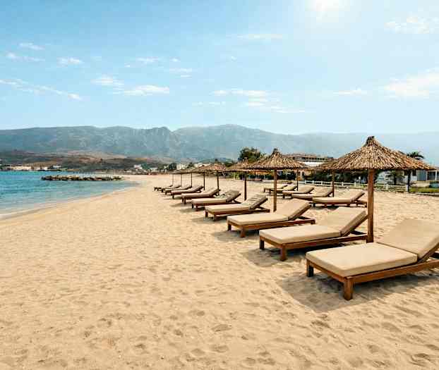 En sandstrand med solsenger og parasoller på rad foran havet. (AI-generert tekst)