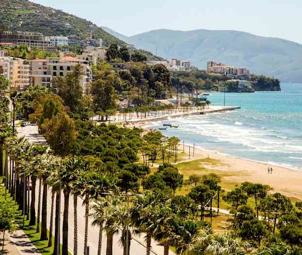 Utsikt over en kystlinje med sandstrand, frodige trær og bygninger i bakgrunnen. (AI-generert tekst)