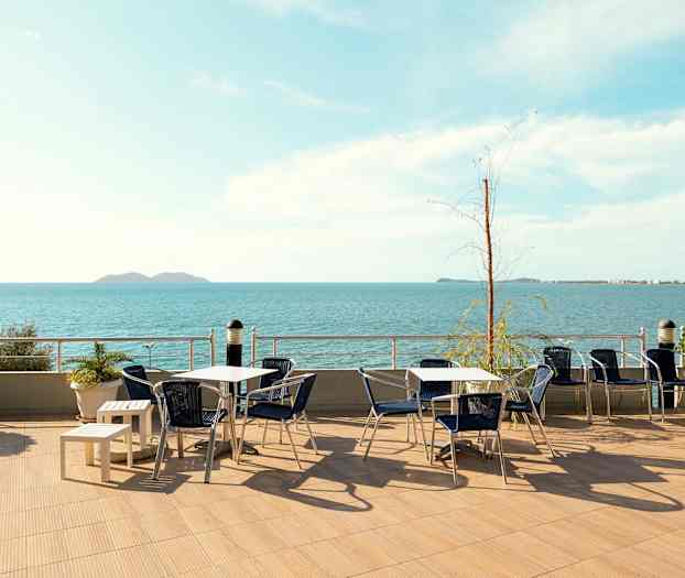En uteplass med bord og stoler og utsikt over havet. (AI-generert tekst)