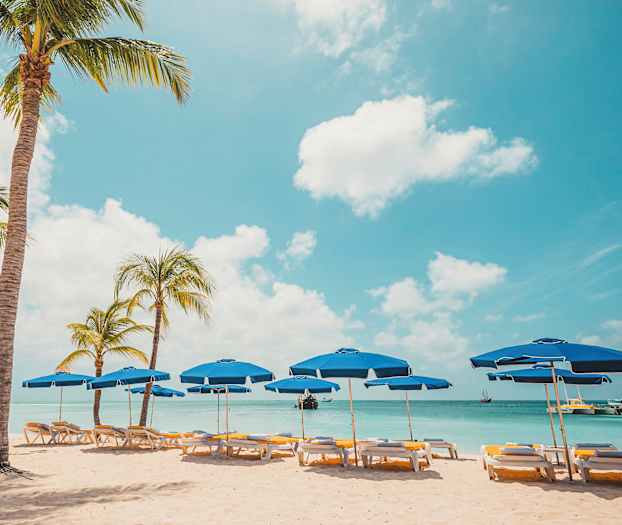 Strand med palmer og blå parasoller ved vannet. (AI-generert tekst)