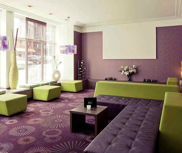 Et lyst rom med lilla vegger og teppegulv, grønne sitteplasser og store vinduer. (AI-generert tekst)
