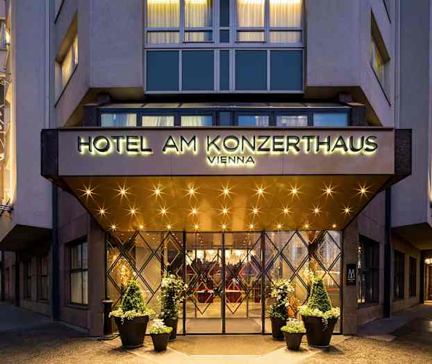 Inngangen til et hotell med et skilt som lyder "Hotel am Konzerthaus Vienna". Belysning og dekorasjoner er synlige rundt inngangen og på fasaden. (AI-generert tekst)
