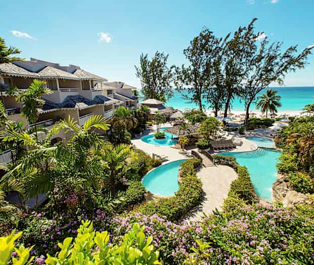 Bilde som viser hotellbygninger omgitt av grøntområder nær et basseng og stranden. (AI-generert tekst)