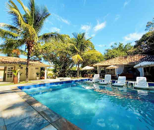 Et svømmebasseng omgitt av solsenger, parasoller og palmer ved en bygning i solrikt vær. (AI-generert tekst)