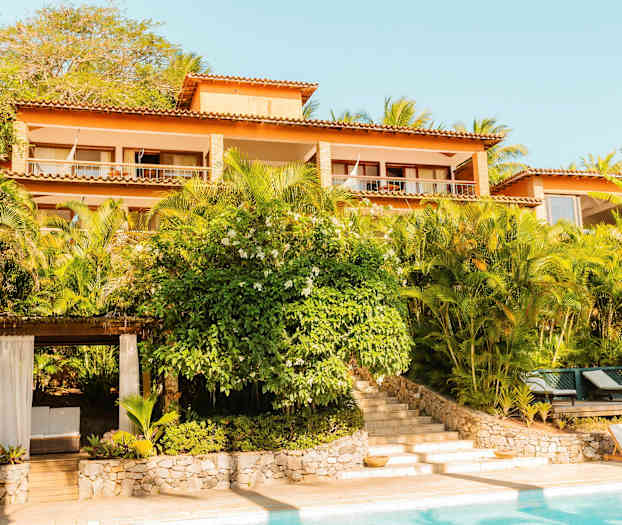 Bilde av en bygning med flere etasjer omgitt av frodige planter, med et basseng i forgrunnen. (AI-generert tekst)