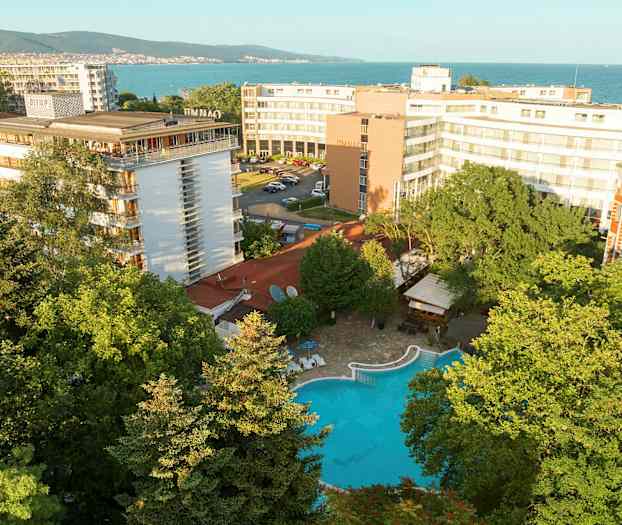 Hotellbygninger med et basseng omgitt av grøntområder, nær havet. (AI-generert tekst)