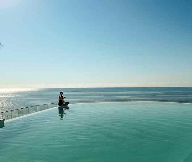 En person sitter ved kanten av et basseng med havet i bakgrunnen. (AI-generert tekst)