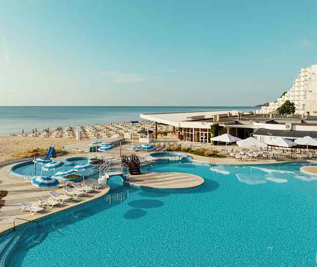 Et bilde av et basseng, solsenger og parasoller ved et hotell nær en sandstrand. (AI-generert tekst)