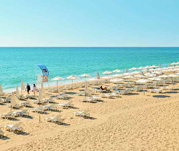 En strand med solsenger og parasoller nær havet. (AI-generert tekst)