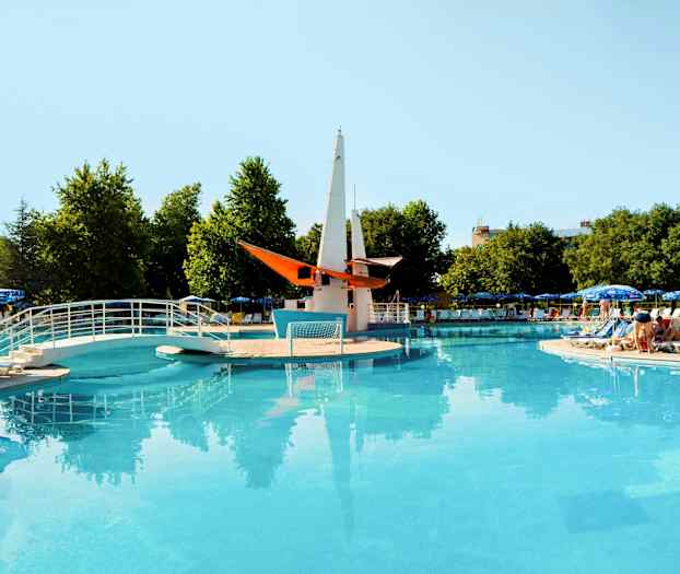 Åpent basseng med bro og dekorativ båt i midten, omgitt av solsenger og parasoller. (AI-generert tekst)