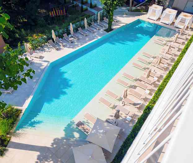 Et bilde av et basseng med solsenger og parasoller rundt i et utendørsmiljø. (AI-generert tekst)