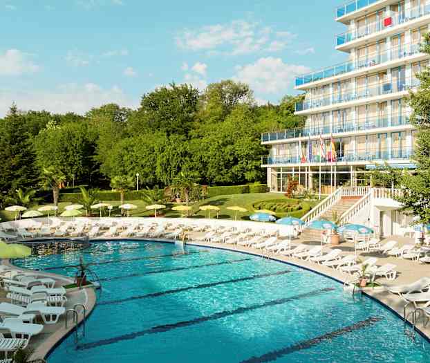 Et basseng omgitt av solsenger og parasoller nær et hotell med flere etasjer. (AI-generert tekst)