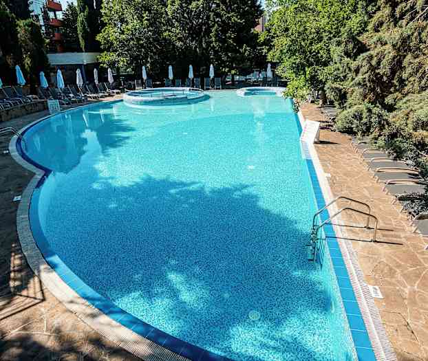 Utendørs basseng omgitt av solsenger og trær. (AI-generert tekst)