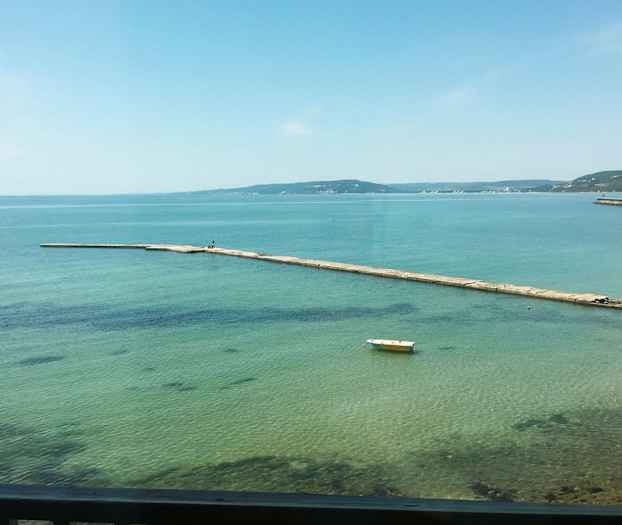 En brygge strekker seg ut i det klare blå vannet. En enslig båt ligger fortøyd ved overflaten. (AI-generert tekst)