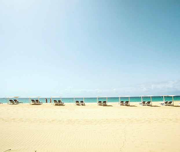 Strand med solsenger og parasoller foran havet. (AI-generert tekst)