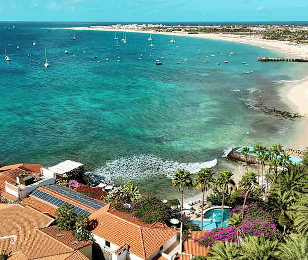 Utsikt over kyst med palmer, turkist vann og seilbåter. (AI-generert tekst)