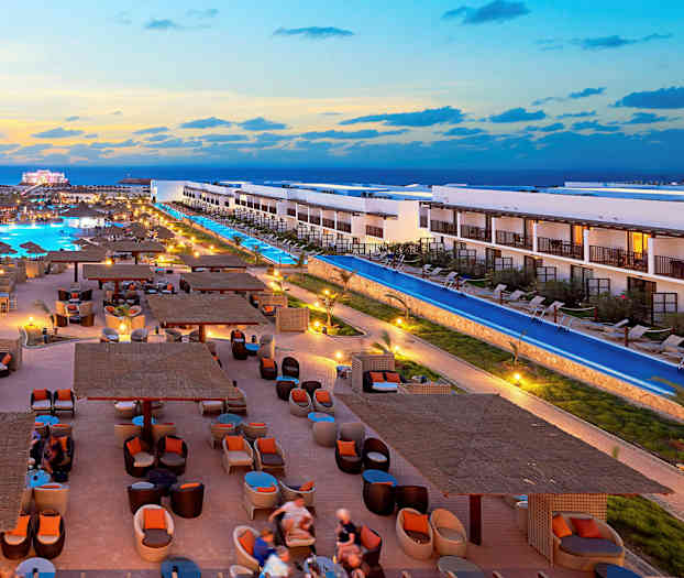 Et hotellområde med bassenger, elegante sitteplasser og bygninger ved solnedgang. (AI-generert tekst)