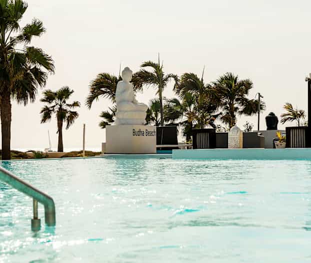 Et utendørsbasseng med en sittende statue og omkringliggende pergolaer og palmer. (AI-generert tekst)