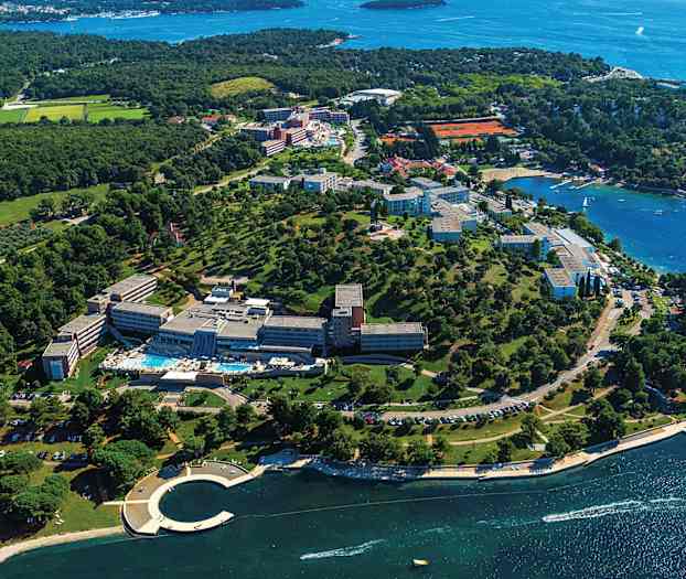 Luftfoto av et ferieanlegg ved kysten med grønne omgivelser og utsikt over havet. (AI-generert tekst)