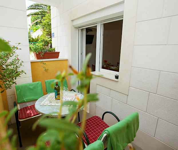 En uteplass med bord, grønne stoler og vindu til et rom. (AI-generert tekst)