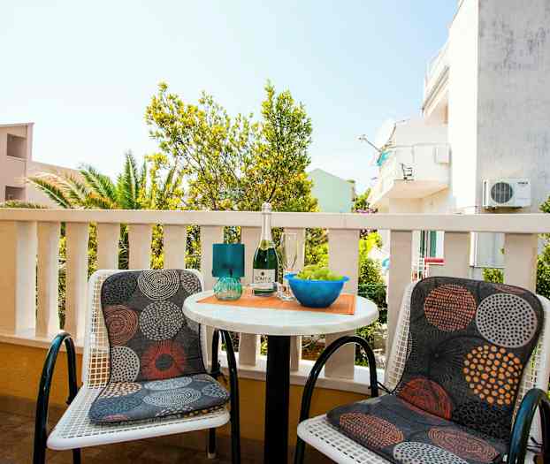 To stoler med mønstrede puter står ved et lite rundt bord på en terrasse med utsikt over omgivelser og vegetasjon. (AI-generert tekst)