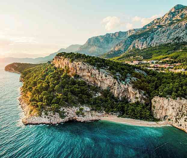 En kystlinje med bratte klipper, en skog og klart blått hav. (AI-generert tekst)