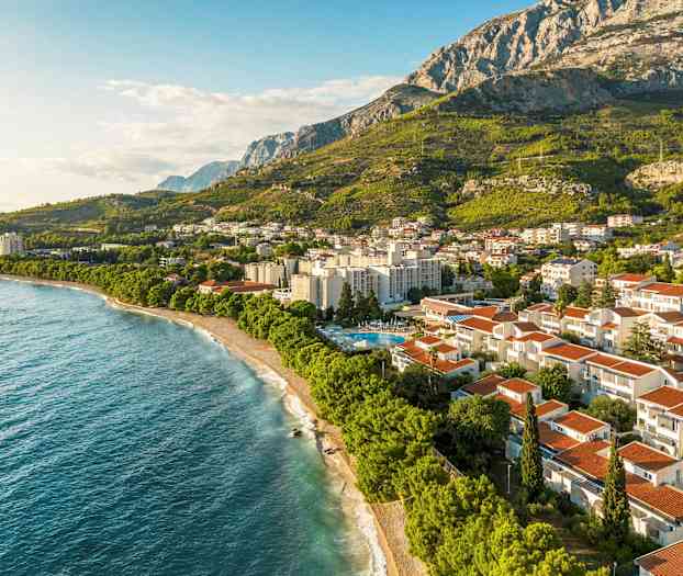 Luftfoto av en kystby foran frodige fjell. (AI-generert tekst)
