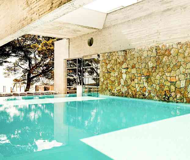 Innendørsbasseng med steinvegg og utsikt mot trær utenfor. (AI-generert tekst)