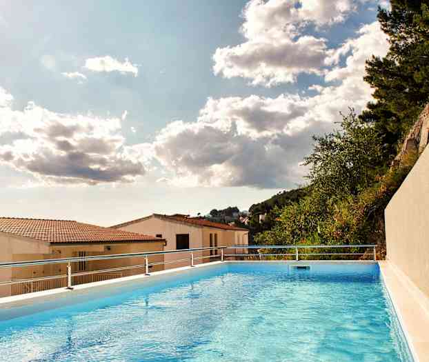 Bilde av et utendørsbasseng med utsikt over hustak og trær under en skyet himmel. (AI-generert tekst)