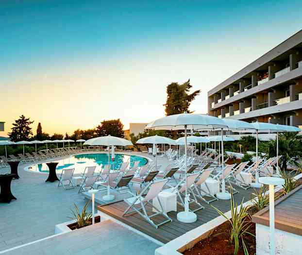 Et hotellbasseområde med solsenger og parasoller i skumringen. (AI-generert tekst)