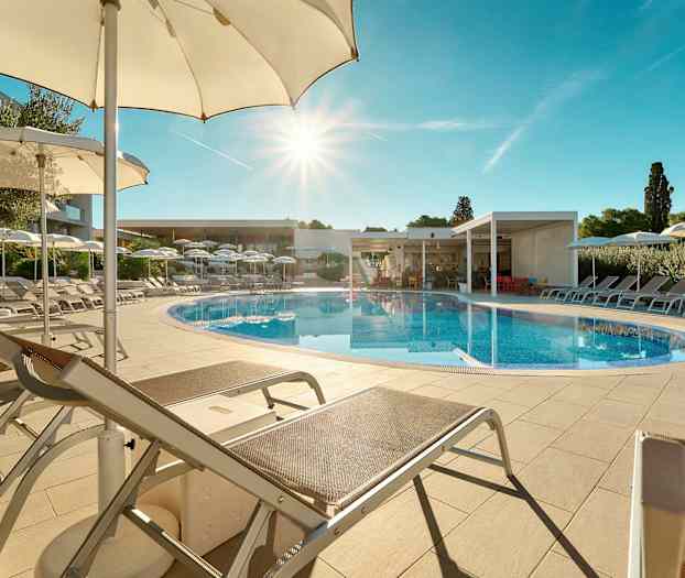 Et utendørs basseng omgitt av solsenger og parasoller under en klar, blå himmel. (AI-generert tekst)