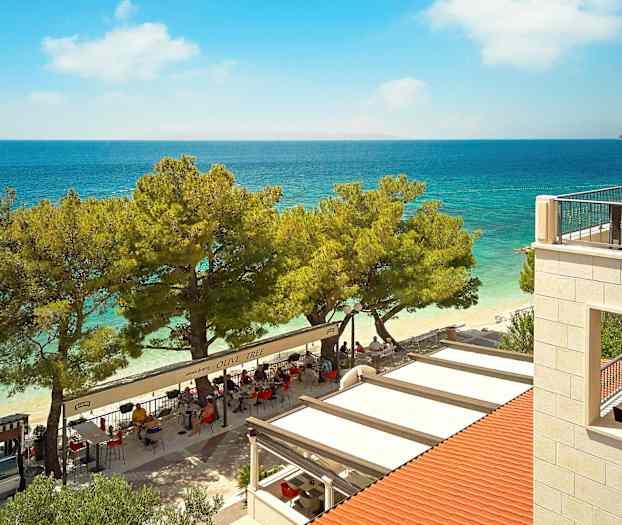 Utsikt over en restaurant ved stranden med havet i bakgrunnen. (AI-generert tekst)