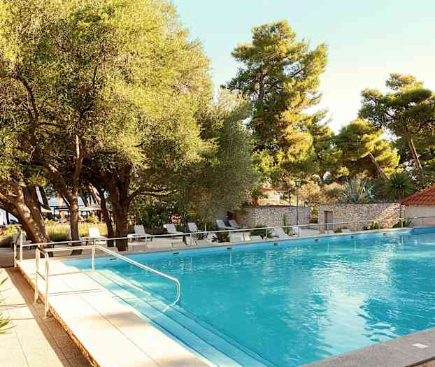 Et utendørs svømmebasseng omgitt av trær og solsenger. (AI-generert tekst)