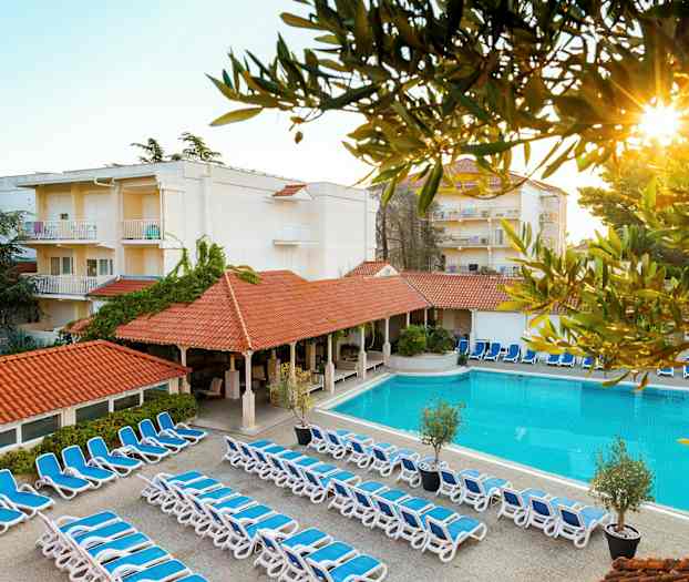 Bilde av hotellområde med solsenger, basseng og bygninger. (AI-generert tekst)