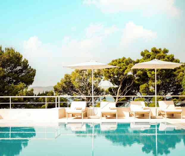 Et utendørsbasseng omgitt av solsenger, parasoller og frodige trær. (AI-generert tekst)