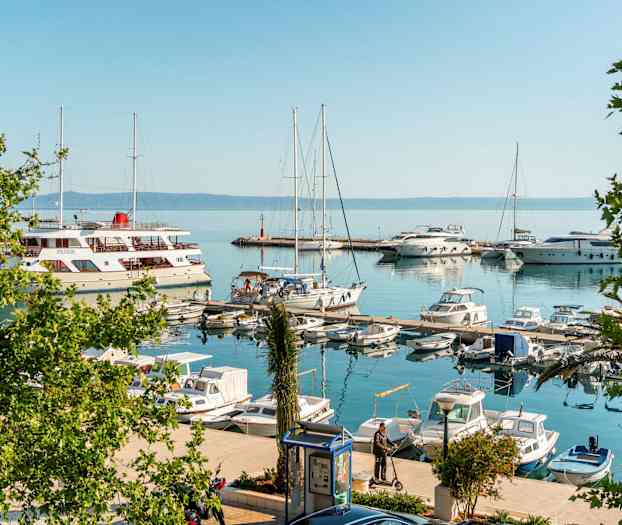 En småbåthavn med seilbåter og motorbåter. Enkelte personer står ved bryggene. (AI-generert tekst)