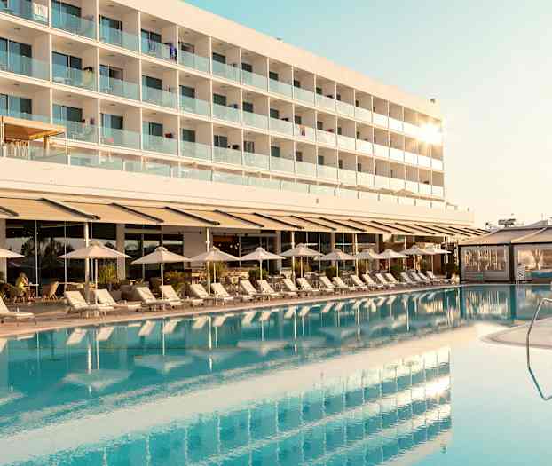 En hotellbygning med balkonger kan sees bak et basseng og solsenger. (AI-generert tekst)