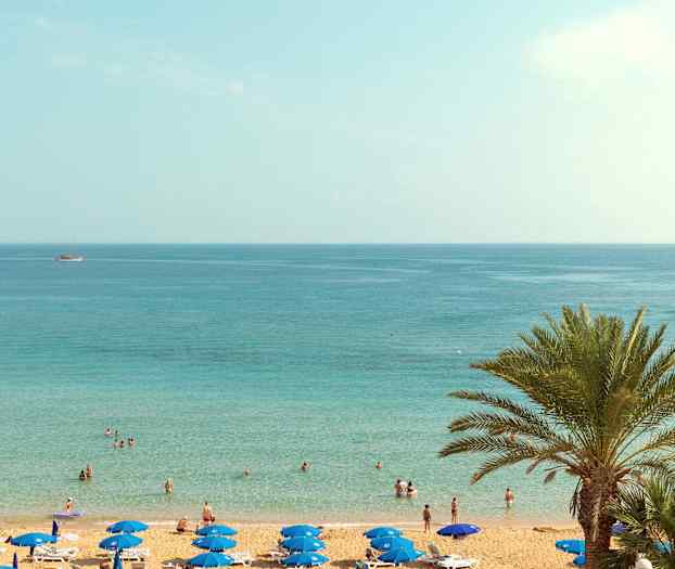 En strand med parasoller og mennesker ved vannet. (AI-generert tekst)