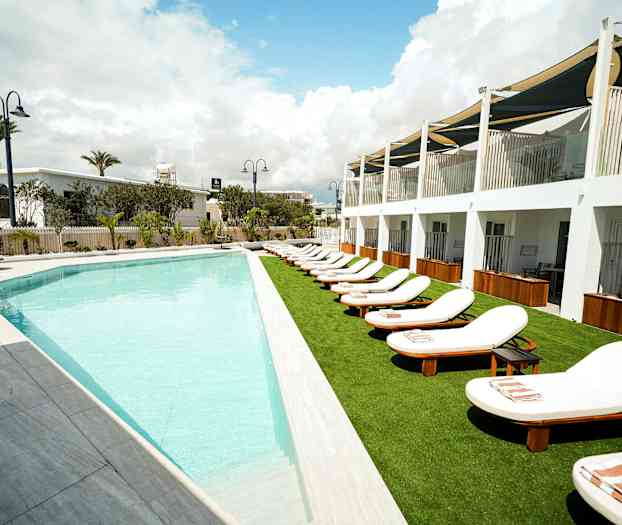 Utendørsbasseng med solsenger ved en hotellbygning. (AI-generert tekst)