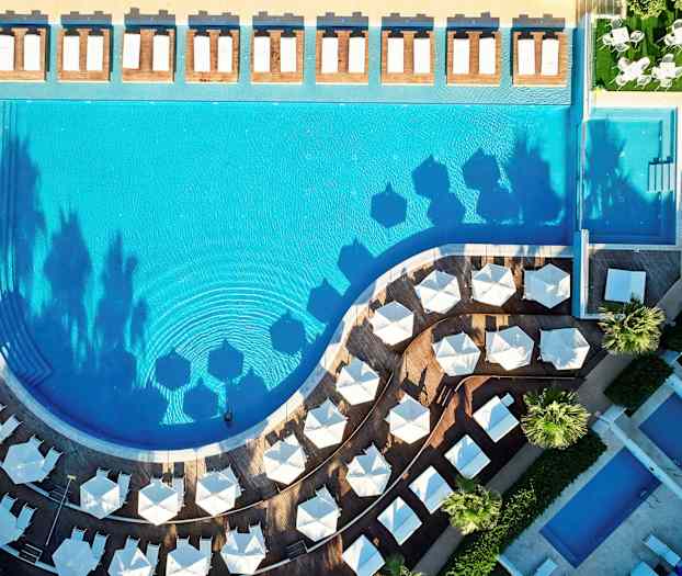 Fugleperspektiv av et basseng med solsenger og parasoller rundt. (AI-generert tekst)