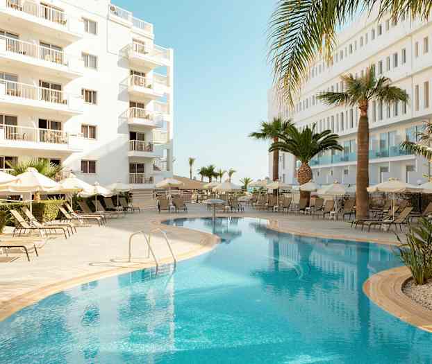 Utendørsbasseng med solsenger og parasoller, omgitt av hvite bygninger og palmer. (AI-generert tekst)