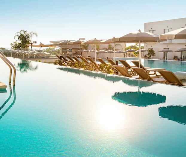 Et utendørsbasseng med solsenger og parasoller ved siden av. (AI-generert tekst)