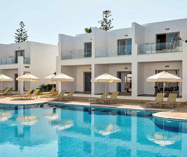 Hvite bygninger med terrasser ved bassengområde med solsenger og parasoller. (AI-generert tekst)