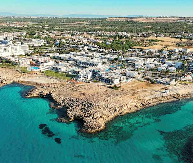 Flyfoto av kystlandskap med turkist vann og bygninger ved stranden. (AI-generert tekst)