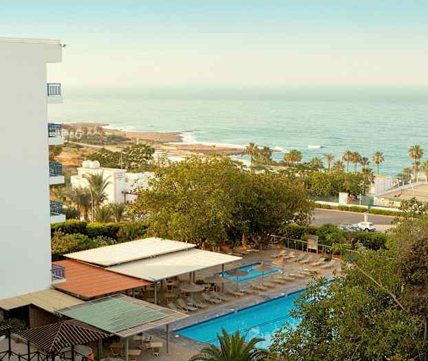 Hotellområde med basseng, solsenger og havutsikt. (AI-generert tekst)